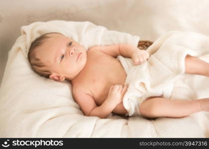 Cute naked caucasian baby boy lying under blanket on bed