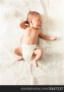 Cute newborn baby boy in diapers lying on white sheets on bed