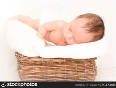 Cute newborn baby boy sleeping in old wicker basket covered by blanket