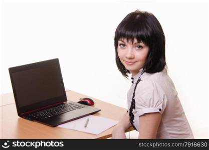 Cute office girl sitting at a table with a laptop in white blouse. The girl at the table with a laptop