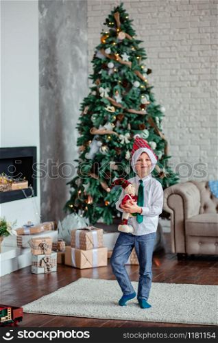 Cute one boy unpacks gifts under the Christmas tree, sitting by the fireplace, on Christmas morning. Merry Christmas.. Cute one boy unpacks gifts under the Christmas tree, sitting by the fireplace, on Christmas morning.