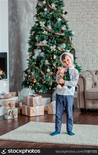 Cute one boy unpacks gifts under the Christmas tree, sitting by the fireplace, on Christmas morning. Merry Christmas.. Cute one boy unpacks gifts under the Christmas tree, sitting by the fireplace, on Christmas morning.