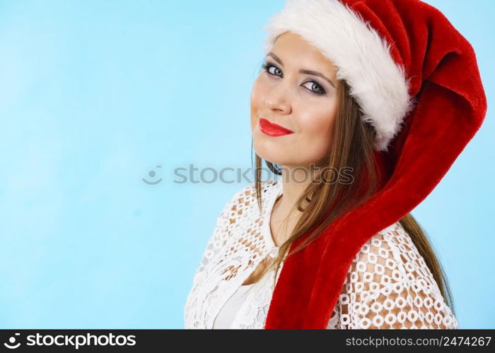 Cute oung woman wearing Santa Claus red hat having fun. Pretty lady is ready for Christmas Holiday season. Blue background.. Cute pretty woman in Christmas Santa hat