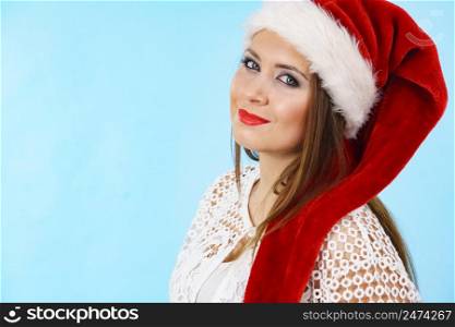 Cute oung woman wearing Santa Claus red hat having fun. Pretty lady is ready for Christmas Holiday season. Blue background.. Cute pretty woman in Christmas Santa hat