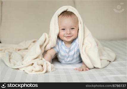 Cute portrait of smiling baby boy lying on bed under white blanket