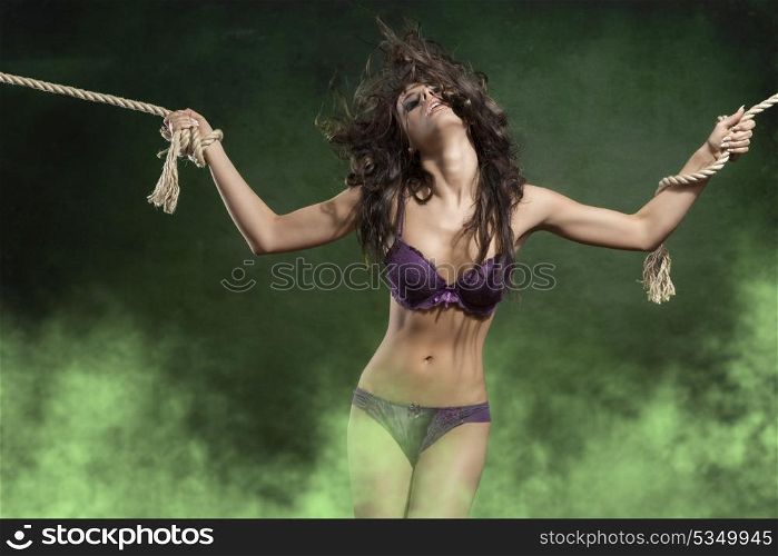 cute portrait of very pretty girl with sensual body, wild flying hair and purple underwear. She is tied by rope