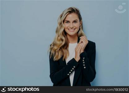 Cute positive female student in stylish casual outfit posing against blue studio wall, looking happily at camera and expressing positivity. Beautiful and happy young people concept. Cute positive female student in stylish casual outfit posing against blue studio wall
