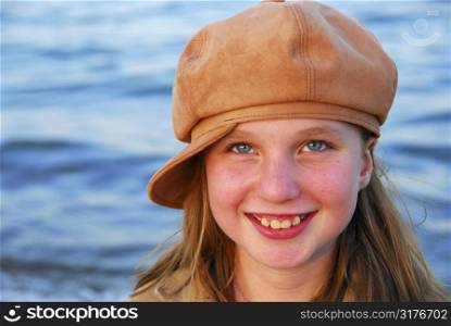 Cute preteen girl smiling wearing suede hat, blue water background