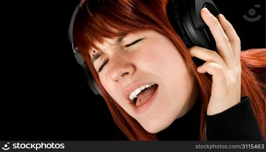 Cute redhead girl enjoying and singing music on her headphones. Studio shot.
