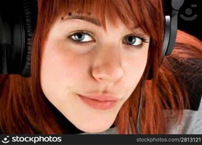 Cute redhead girl looking seductively at camera, smiling, and listening to music on headphones. Studio shot.
