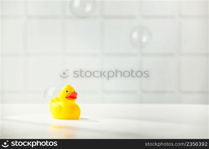 Cute rubber duck on white bathroom countertop with soap bubbles, space for text, horizontal composition