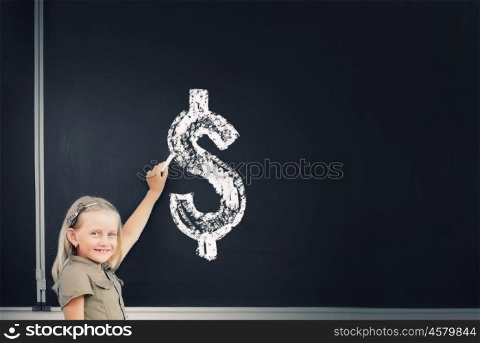 Cute school girl drawing dollar sign on blackboard. Girl at blackboard