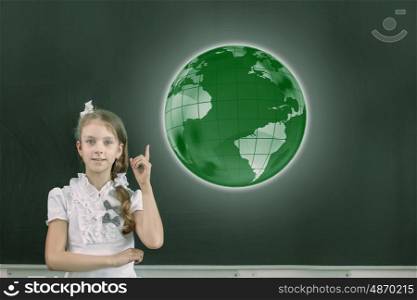 Cute school girl pointing at globe above her head. At geography lesson