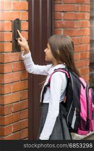 Cute schoolgirl in school uniform ringing in doorbell