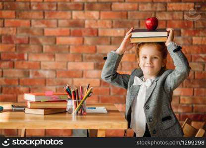 Cute schoolgirl sitting at the table, side view. Female pupil at the desk with textbooks, apples and globe, young girl doing homework. Cute schoolgirl sitting at the table, side view
