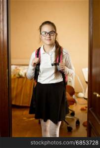 Cute schoolgirl with backpack walking out of her bedroom to school