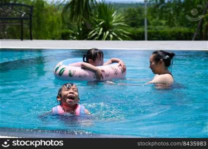 Cute sisters are swimming in life jackets with her mother in the pool on a sunny day. Happy family, mother and her daughters playing in the swimming pool. Summer lifestyle concept.