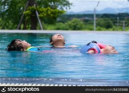 Cute sisters are swimming in life jackets with her mother in the pool on a sunny day. Happy family, mother and her daughters playing in the swimming pool. Summer lifestyle concept.