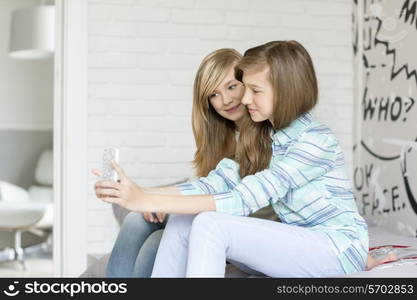 Cute sisters photographing themselves through cell phone at home