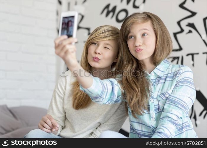 Cute sisters pouting while taking photos with smart phone at home