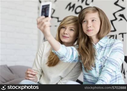 Cute sisters taking photos with smart phone at home