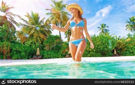 Cute slim female wearing stylish blue swimsuit comes into sea, enjoying summer vacation on Maldives island, joy and fun concept