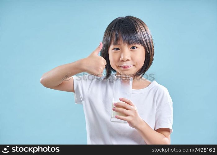 Cute smart asian little girl say good while drinking milk on blue background