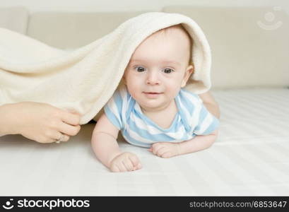 Cute smiling 6 month baby boy lying under the blanket on bed