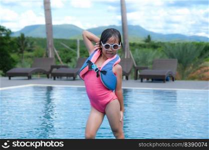 Cute smiling Asian little girl in sunglasses stands sexy pose by the pool on a sunny day. Summer lifestyle concept.