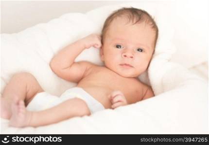 Cute smiling baby boy lying on soft beige blanket and cushion