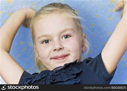 Cute smiling blond girl on blue background with upwards hands