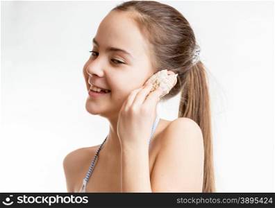 Cute smiling girl holding seashell next to ear and listening to ocean
