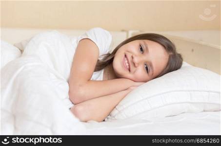 Cute smiling girl lying on pillow and looking at camera