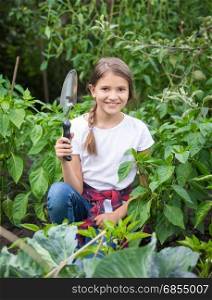 Cute smiling girl posing with trowel at blooming garden