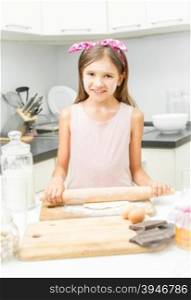 Cute smiling girl rolling dough on messy kitchen