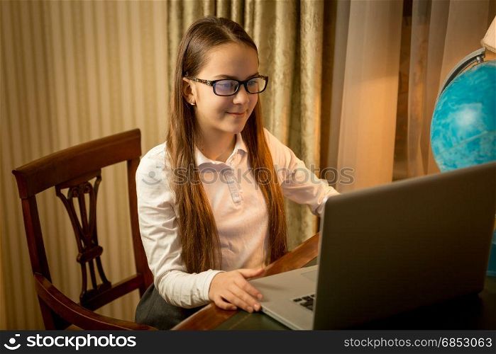 Cute smiling girl typing message on laptop
