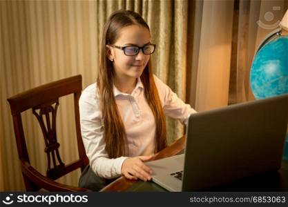 Cute smiling girl typing message on laptop