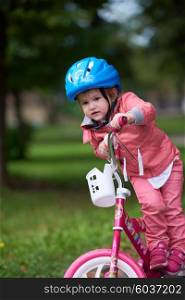 Cute smiling little girl with bicycle and helmet on road in the park