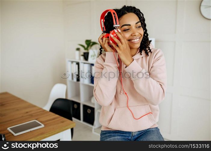 Cute smiling woman in headphones enjoys listening to music. Pretty lady in earphones relax in the room, female sound lover resting. Cute smiling woman enjoys listening to music