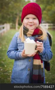 Cute Smiling Young Girl Wearing Hat and Scarf Holding Cocoa Mug with Marsh Mallows Outside.