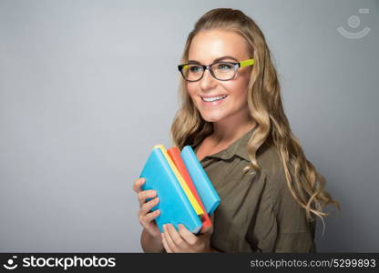 Cute student girl portrait, wearing grasses and standing with books over gray background, ready to new study season, enjoying education in a college
