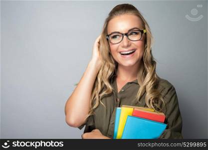 Cute student girl wearing grasses, standing with textbooks over gray background, ready to new study season, enjoying education in a college