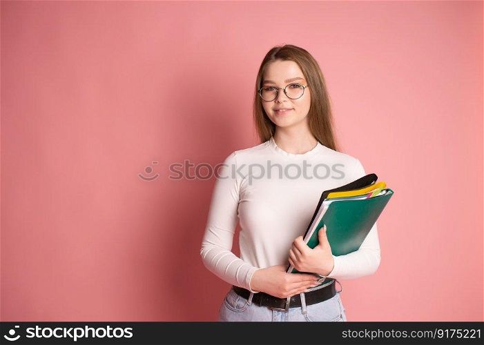 Cute student girl with glasses holds folders on pink background.. Cute student with glasses holds colorful folders on a pink background