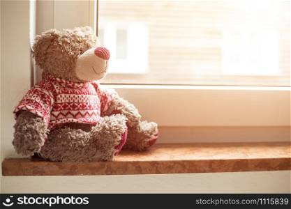 Cute teddy bear is sitting on the windowsill, looking out of the window