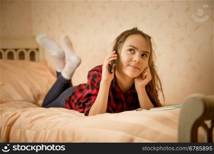 Cute teenage girl lying in bedroom and talking by phone