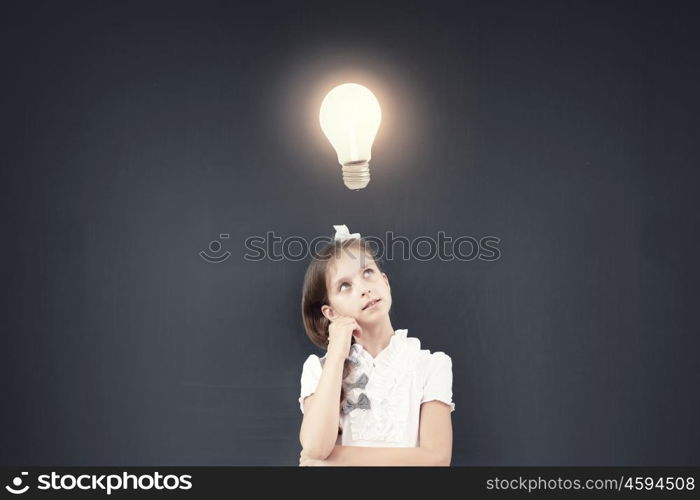 Cute thoughtful girl of school age standing near blackboard. Back to school