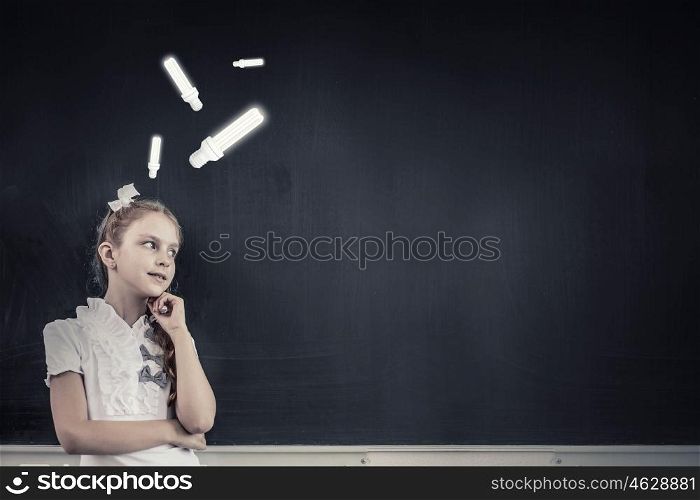 Cute thoughtful girl of school age standing near blackboard. Back to school