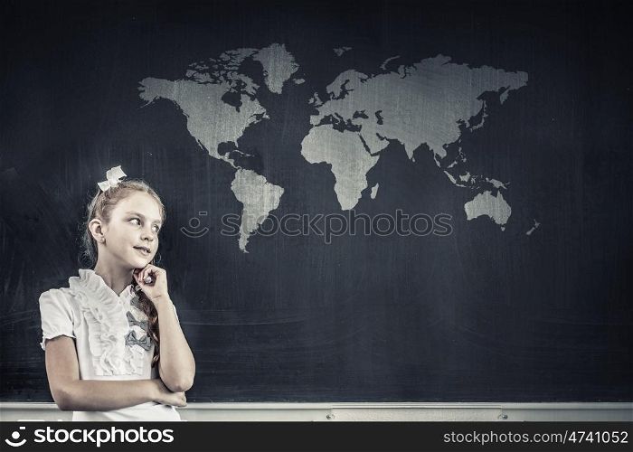 Cute thoughtful girl of school age standing near blackboard. Back to school