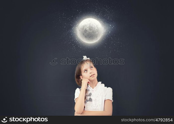 Cute thoughtful girl of school age standing near blackboard. Back to school