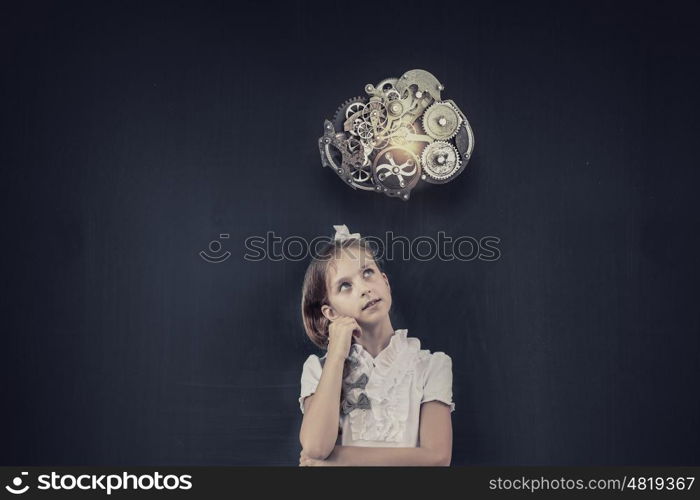 Cute thoughtful girl of school age standing near blackboard. Back to school